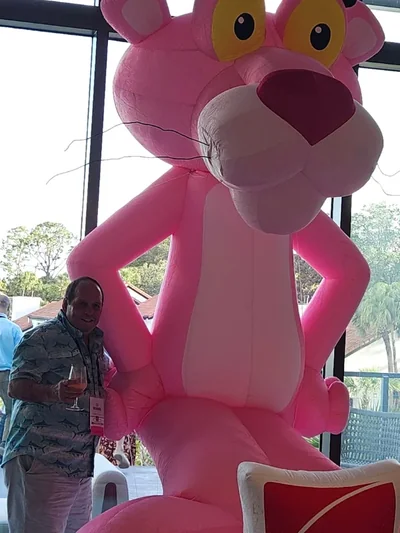 Ed Richards smiling and posing with the CEE, Owens Corning Pink Panther mascot.