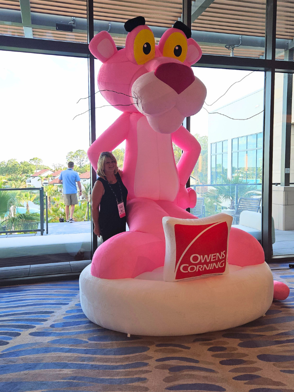 Michelle Richards smiling and posing with the CEEE, Owens Corning Pink Panther mascot.