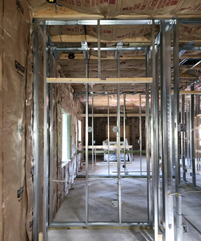 R-30 kraft-faced fiberglass batts (Owens Corning "PINK Next Gen Firebatt" visible on packaging) installed in ceiling joists of a new construction commercial or mixed-use build, with Fi-Foil radiant barrier on the walls. Metal stud framing throughout. Original filename confirms Fort Pierce location.