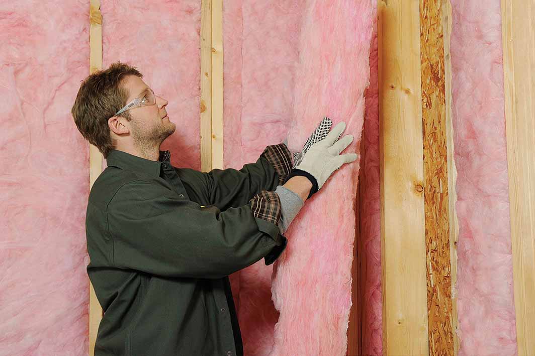 Installer placing Owens Corning EcoTouch fiberglass insulation in a residential wall cavity for improved energy efficiency and comfort.