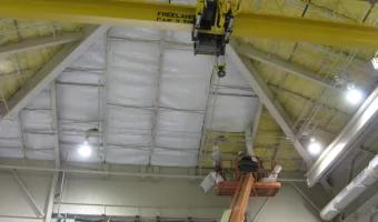 contractors on a lift installing insulating on the ceiling of a large metal building