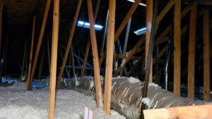 The interior of a FL home attic filled with thick, white blown-in insulation and large silver HVAC ducts running between wooden roof trusses.